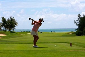 A golfer swinging a golf club on a lush green course, highlighting the importance of preventing and managing back pain while playing golf.