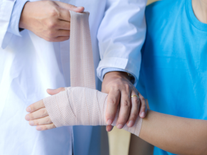 A doctor wrapping an elastic bandage around a patient's hand and wrist, demonstrating the proper use of supportive bandages for injury recovery.