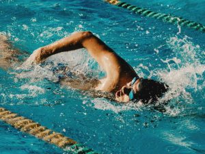 A swimmer performing a freestyle stroke in a pool, highlighting the use of waterproof kinesiology tape for improved performance and injury prevention