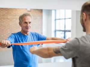 An elderly man practicing resistance band exercises with a trainer, showcasing how exercise bands are used for physical therapy and rehabilitation.