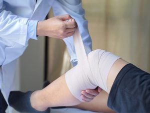 A healthcare professional applying compression therapy on a patient’s knee using an elastic bandage to reduce swelling and improve circulation. Suitable for conditions like lymphedema, venous leg ulcers, or post-injury rehabilitation.