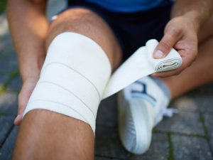 A person wrapping their knee with a 3M elastic adhesive bandage, providing support and compression for joint stabilization. The bandage is suitable for injuries or medical purposes and adheres effectively to the skin