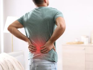 Image of a man holding his lower back after using a traditional pillow. Now he is considering an orthopaedic pillow to relieve back pain.