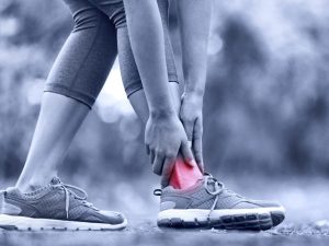 A person holding their injured ankle with a highlighted red area, emphasizing the importance of kinesiology athletic tape vs athletic tape for support.