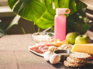 A table with a variety of nutritious foods, including eggs, grains, cheese, fruits, and a hydration bottle, emphasizing the importance of nutrition and hydration for athletes in enhancing sports performance.