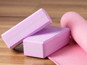 Two pink yoga blocks and a matching yoga mat on a wooden floor, ideal for stretches and lower back support exercises