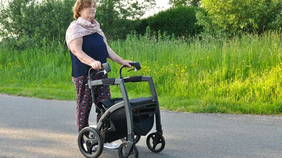 Woman walking in the park using a 4 wheel rollator. She feels comfortable with the choice she made.