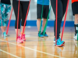 A group of individuals performing a resistance band workout in a gym, focusing on leg and arm exercises using elastic bands for strength and fitness.