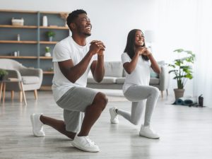 A smiling couple performing lunges in a well-lit living room, showcasing weighted and bodyweight exercises for effective weight loss