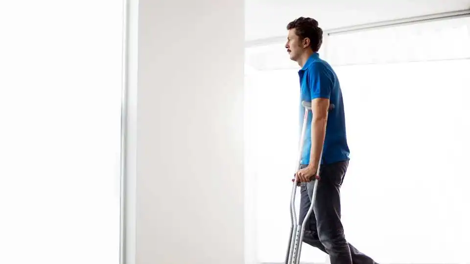 Male wearing a blue shirt has a broken ankle and uses crutches to walk.