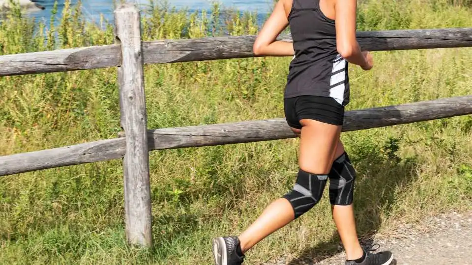 A runner wearing knee supports on both legs jogs confidently on uneven terrain in the countryside.
