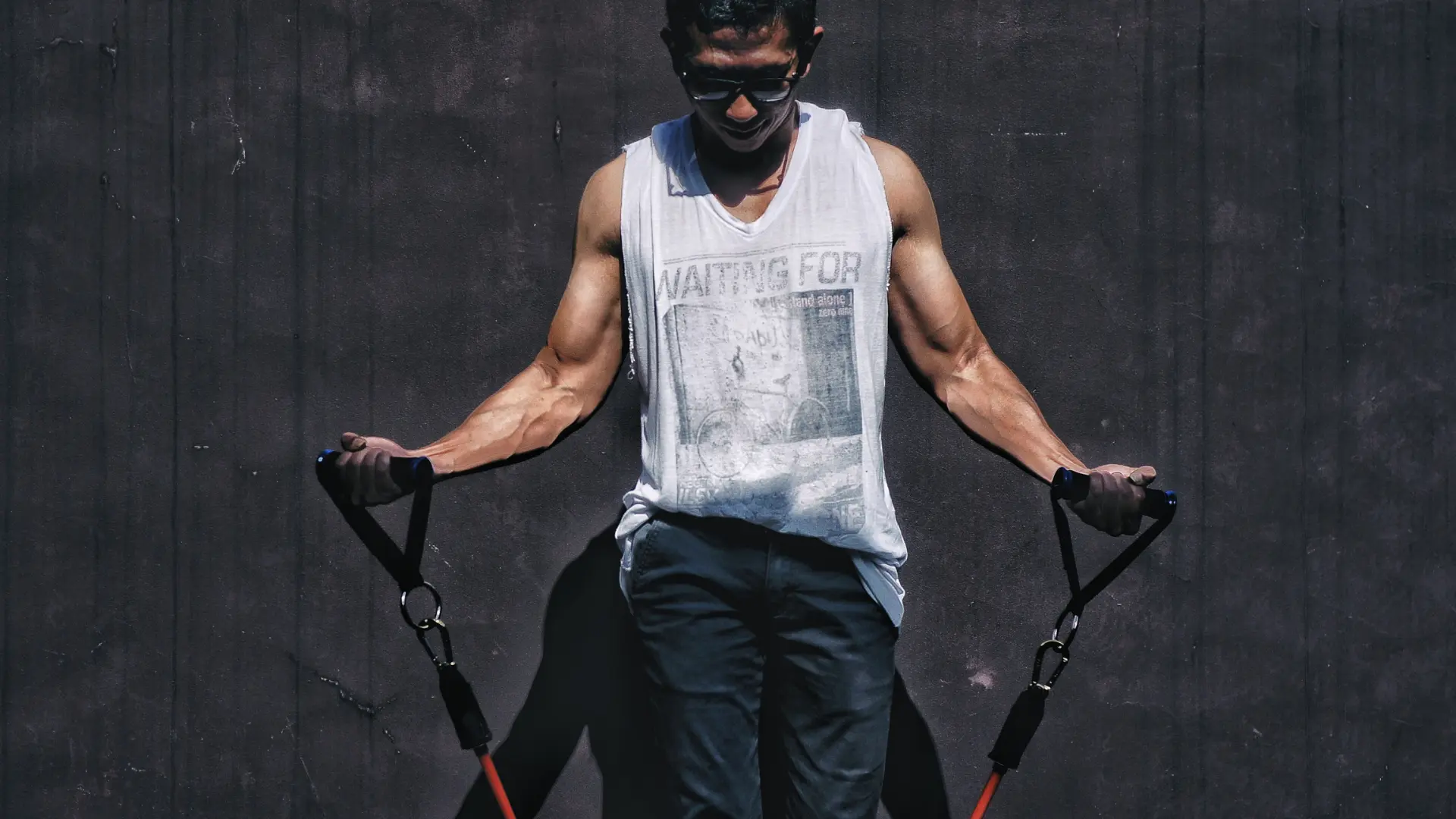 Young athletic male using resistance bands to grow his muscles. He is training his biceps.