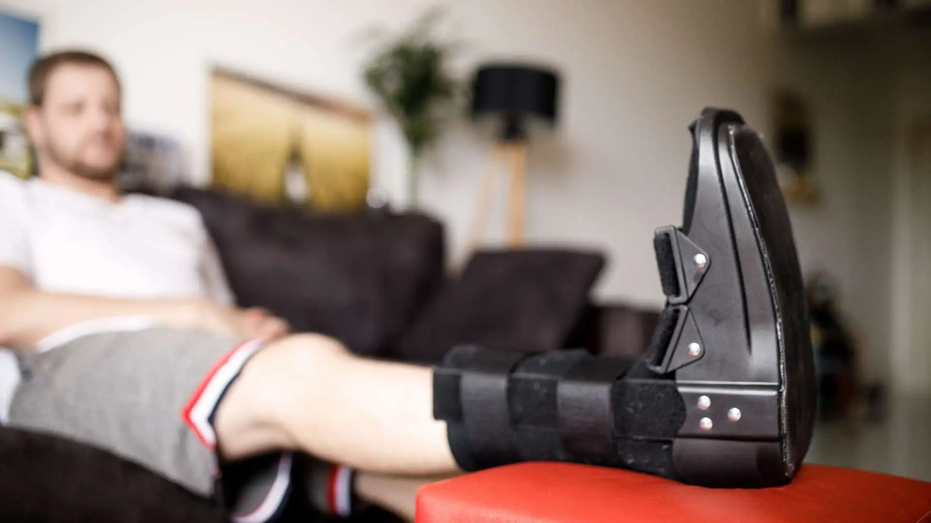 Man sitting on a sofa and resting his broken leg that has an orthopedic boot on.