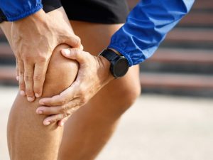 An athlete holding his knee because he is in pain after a run.