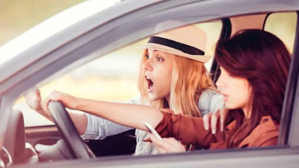 Girl shouting at her friend to be careful while driving as she is distracted by her orthopedic boot and phone.