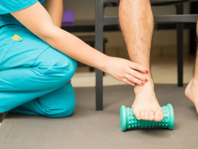 A physio showing a patient how to use a foot roller for plantar fasciitis pain.