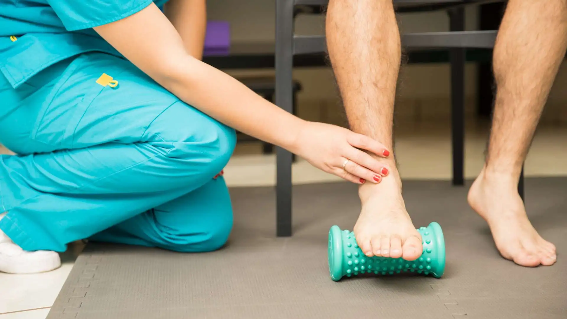 A physio showing a patient how to use a foot roller for plantar fasciitis pain.