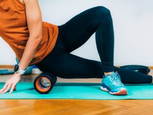 Person using a foam roller on a yoga mat to massage leg muscles and relieve tight calf muscles for improved recovery and pain relief.