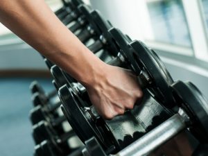 Close-up of a person lifting free weights from a gym rack, highlighting the benefits and differences between free weights and machines for strength training.