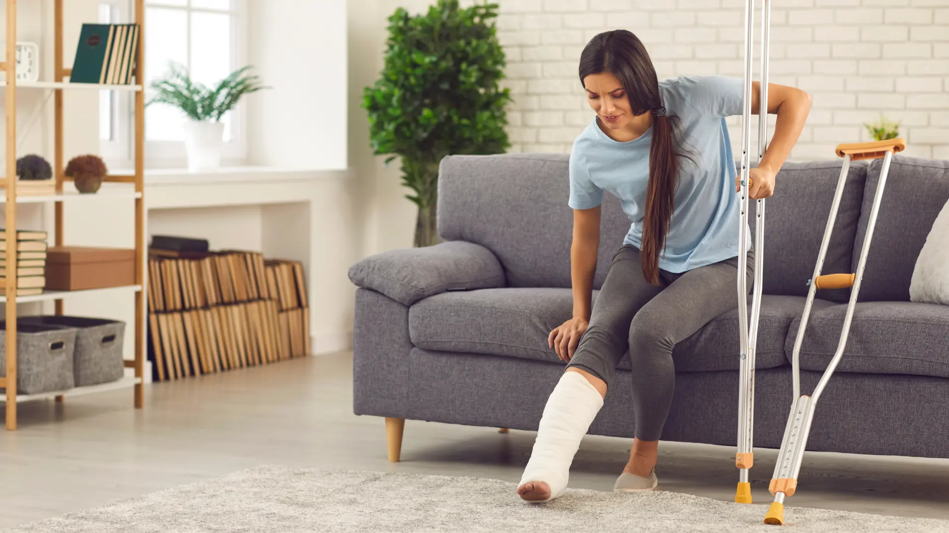 Woman with a broken leg sitting trying to stand up from the sofa using crutches.