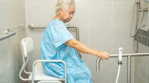 Elderly woman sitting on a shower chair in the bathroom before taking a shower.
