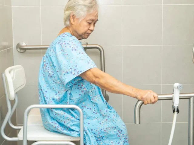 Elderly woman sitting on a shower chair in the bathroom before taking a shower.