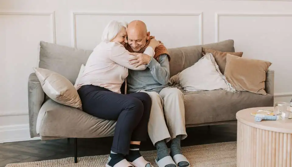 Elderly couple hugging on the sofa. The man can't stand safely but his wife is taking care of him.