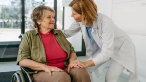 A GP explaining to an elderly woman how to apply for a free wheelchair in Ireland.