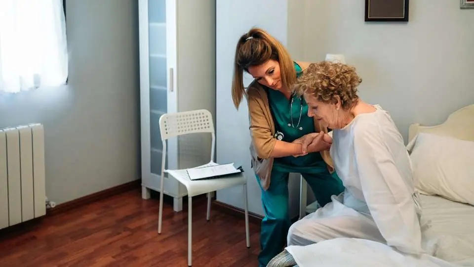 A nurse helping a patient get off the bed to use the toilet and replace the incontinence sheets.