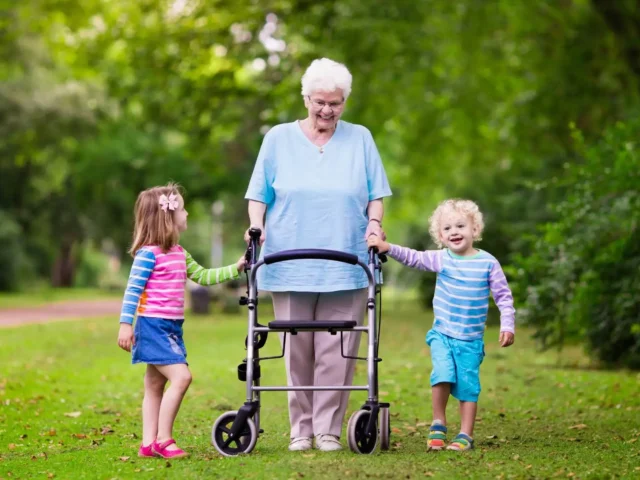 Elderly woman using a rollator and walking in the park with her grandchildren.