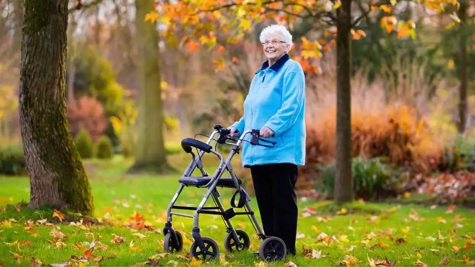 A woman using 4 wheel rollator walker in the park.