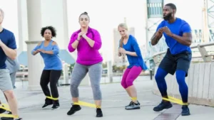 Group of men and women training with resistance bands following instruction from a trainer about toning their legs.