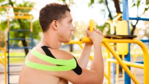 Young male warming up before workout while wearing a yellow and black kinesio tapes on his shoulders.