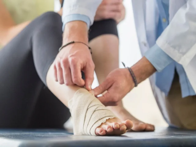 Physio specialist applying bandages to an injured ankle while explaining how comfortable the knee walker is for ankle injuries.