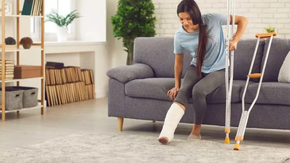 Pregnant woman with a broken leg trying to get up from the sofa using her forearm crutches.