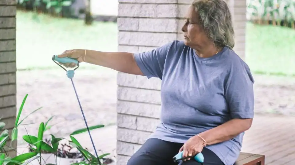 A woman who has difficulties standing is working out with resistance bands while seated on a garden bench.