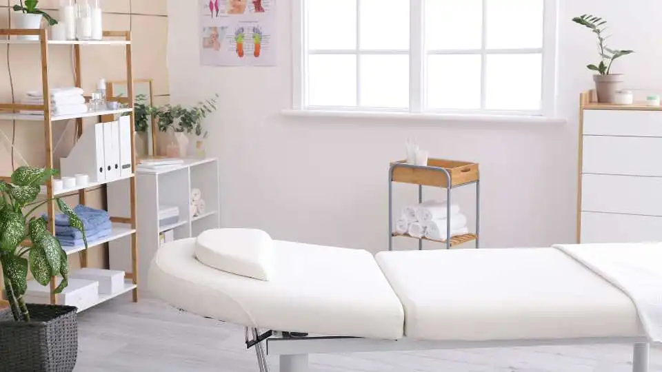 Clean physio cabinet with a white treatment table that have couch roll and spare hand towels on the side.