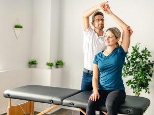 Therapist assisting a patient with shoulder therapy on a portable massage table in a bright and relaxing clinic environment.
