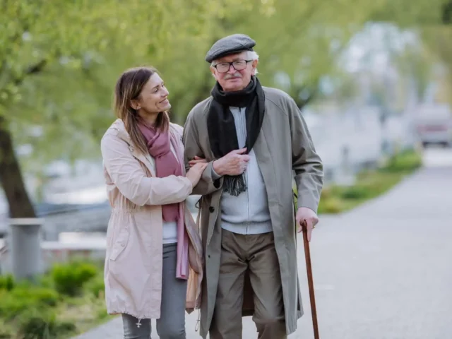 Elderly man using walking stick in the park while walking with his daughter