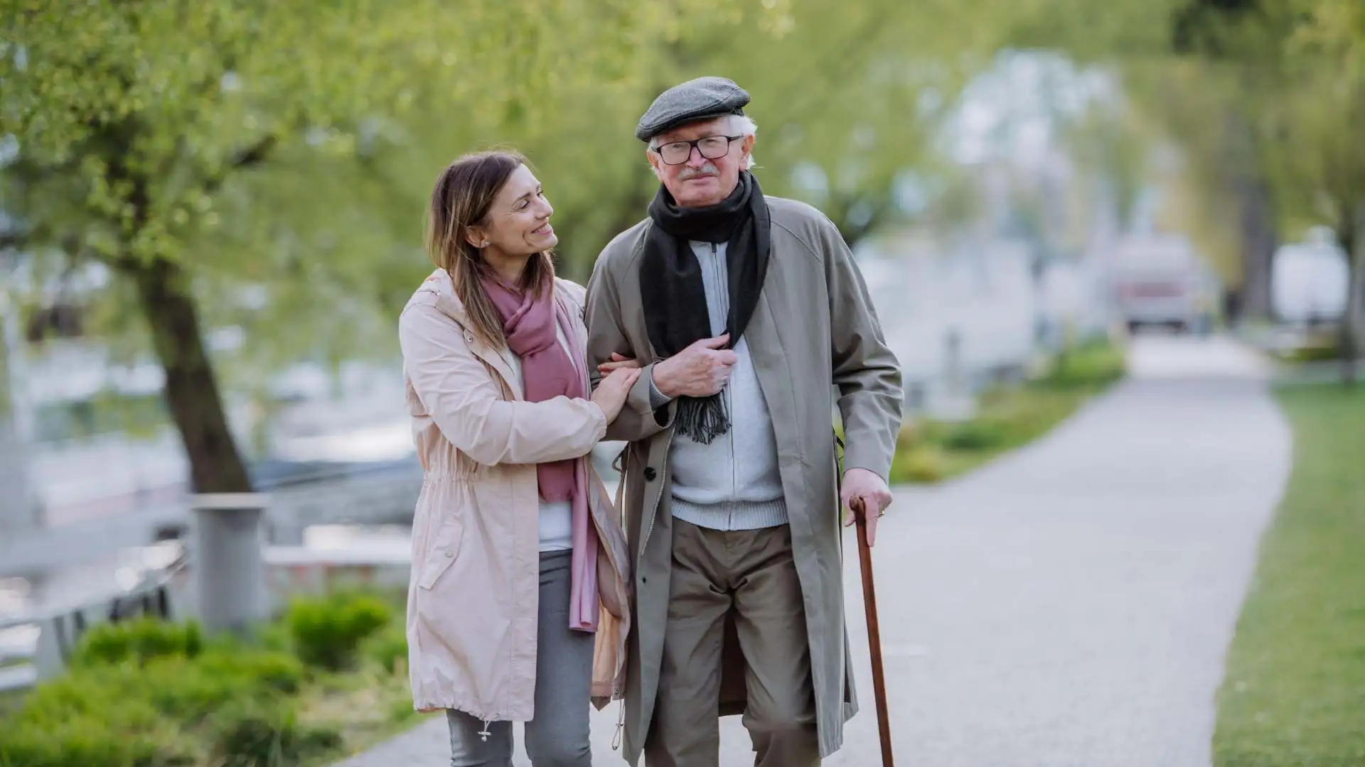Elderly man using walking stick in the park while walking with his daughter
