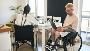 Students using wheelchairs and working on their assignments. They use a manual and an electric wheelchair.