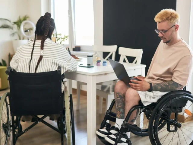 Students using wheelchairs and working on their assignments. They use a manual and an electric wheelchair.