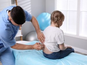A therapist conducting an ergonomic assessment on a child in an occupational therapy session using a treatment table for proper support.