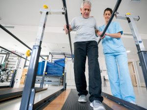 An elderly man receiving rehabilitation support using parallel bars under the guidance of a physiotherapist, showcasing the importance of parallel bars for home and clinical use.