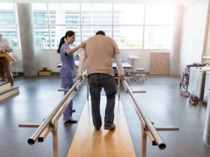 A physiotherapist assisting a patient using rehabilitation parallel bars to restore mobility and balance during therapy.