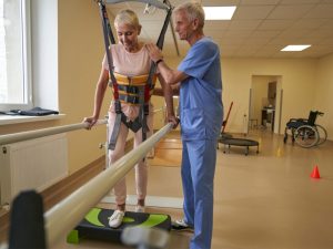 A physiotherapist assisting an elderly woman with gait training exercises using parallel bars in a rehabilitation center.