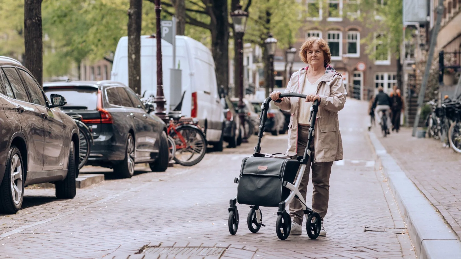 Elderly woman walking in the city pavement using an outdoor rollator walker.