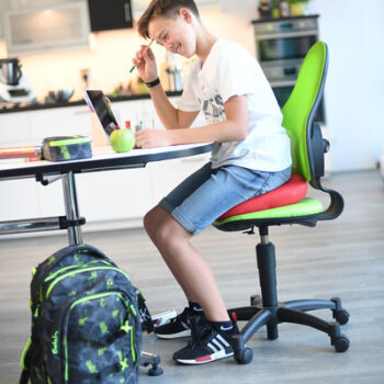 Young boy doing homework while sitting on the Sissel Sitfit Plus Balance Cushion to support posture and focus.