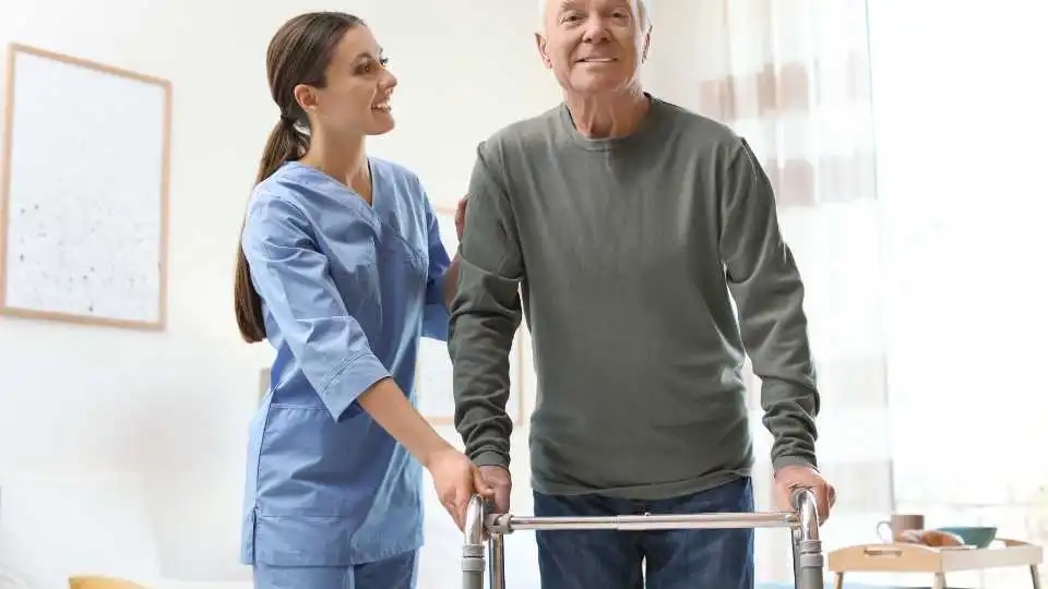 Elderly person using a rollator while supervised by his caregiver at home.