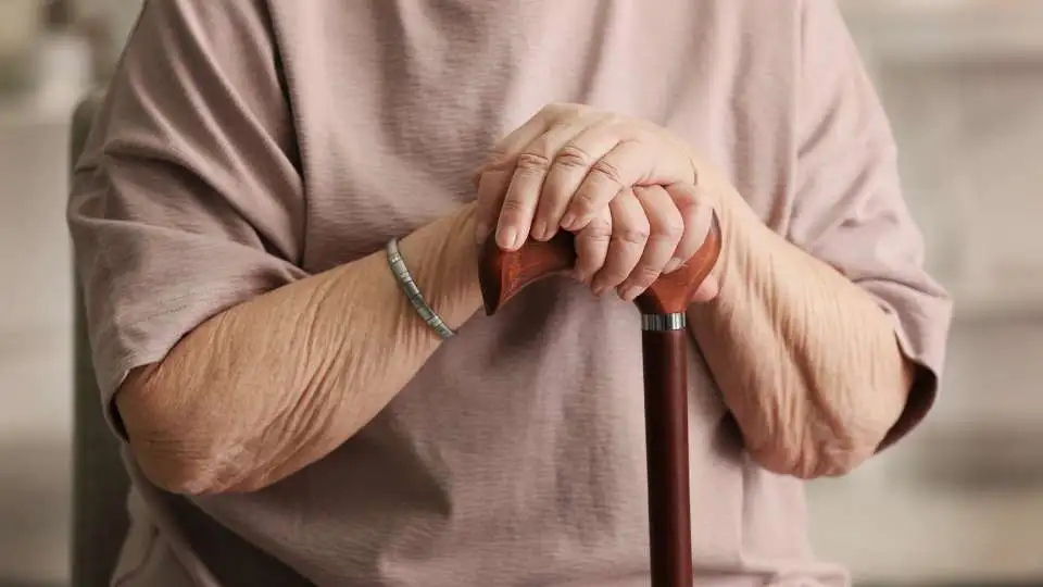 Elderly woman with a single point walking stick at home.